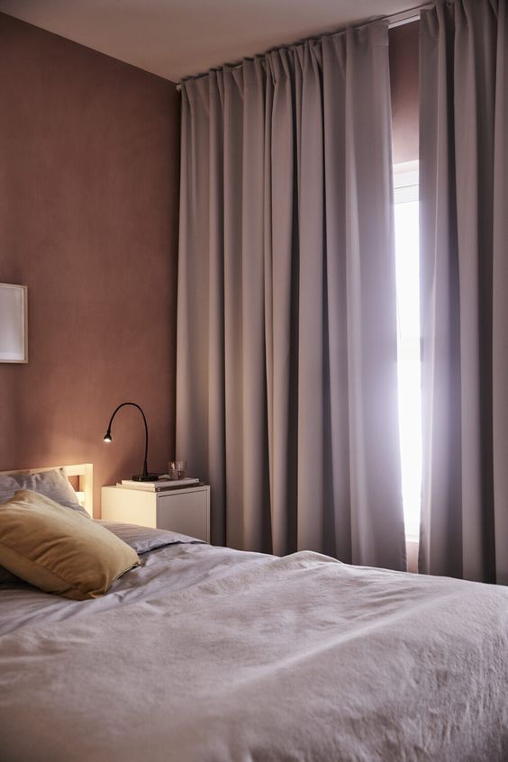 a mauve bedroom with mauve walls, a bed with lavender bedding, lavender curtains and black table lamps