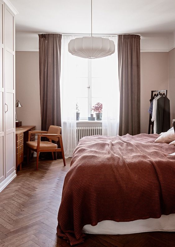 a mauve bedroom with mid-century modern furniture, mauve curtains, burgundy bedding and a paper lamp