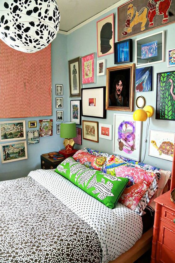 a maximalist gallery wall in various bright colors, with mismatching frames taking two walls looks very bold and cool