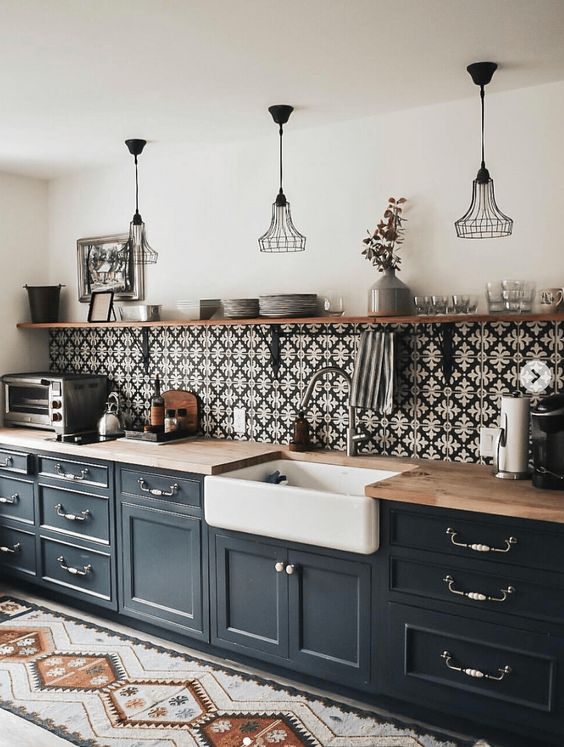 a mid-century modern black one wall kitchen with butcherblock countertops, a patterned tile backsplash and metal pendant lamps