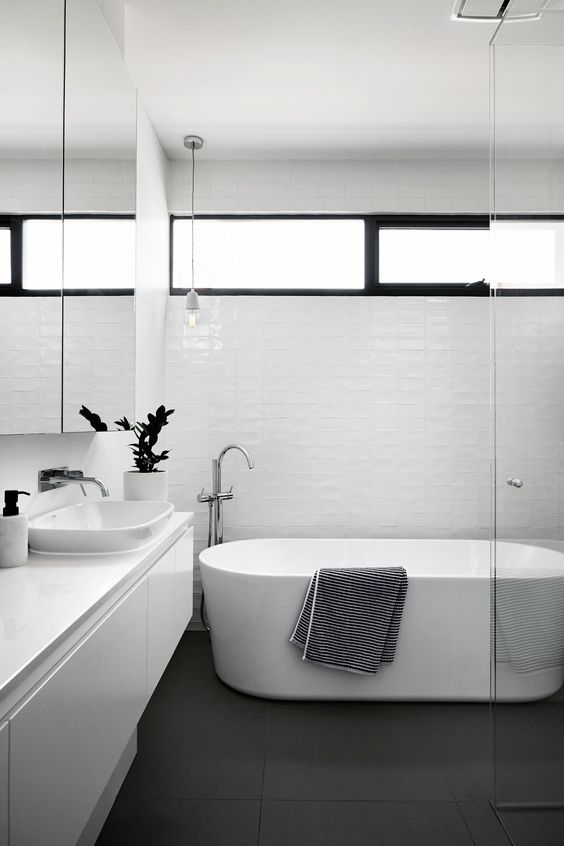 a minimalist bathroom with white tiles and appliances, a clerestory window for light but enough privacy at the same time