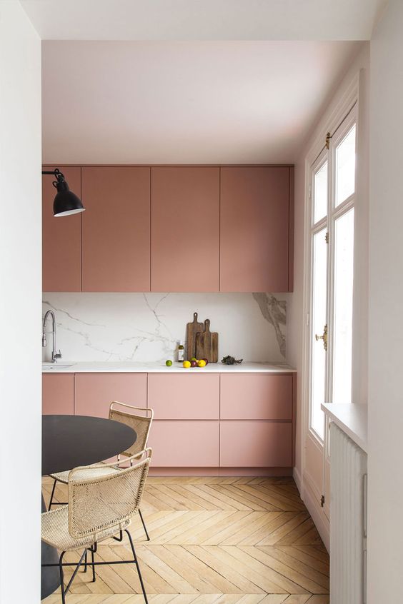 a minimalist mauve kitchen with a white stone backsplash and countertop, a black table and woven chairs