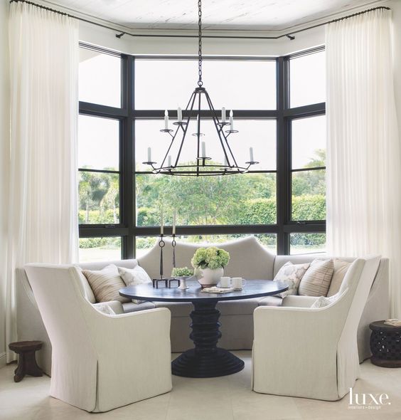 a monochromatic nook at the bow window with black framing, with neutral curtains and a built-in sofa, a black round table