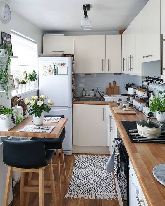 a neutral L-shaped kitchen with grey tiles, butcherblock countertops and potted greenery and blooms