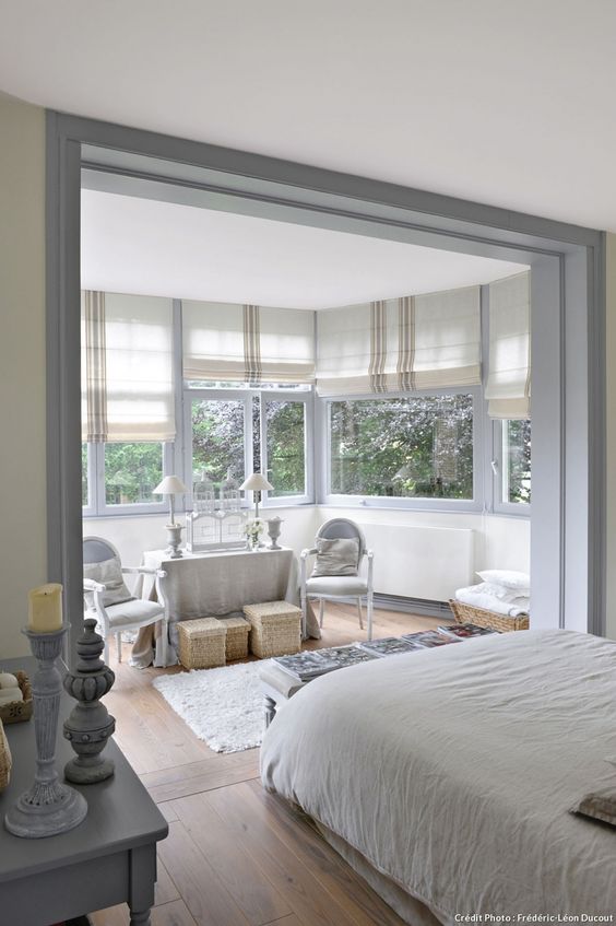 a neutral farmhouse bedroom with a large bow window and a seating nook placed there, the sleeping zone seems separated