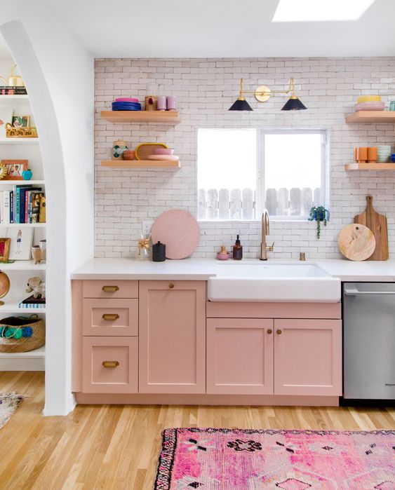 a pretty pink one wall kitchen with a white countertop and a white tile backsplasj, open shelves and colorful tableware