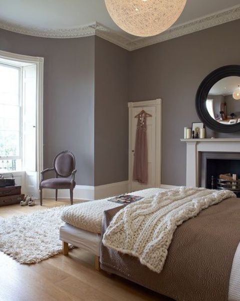a refined Parisian bedroom with mauve walls, a bed, a refined chair, a non working fireplace and a round mirror plus a woven lamp
