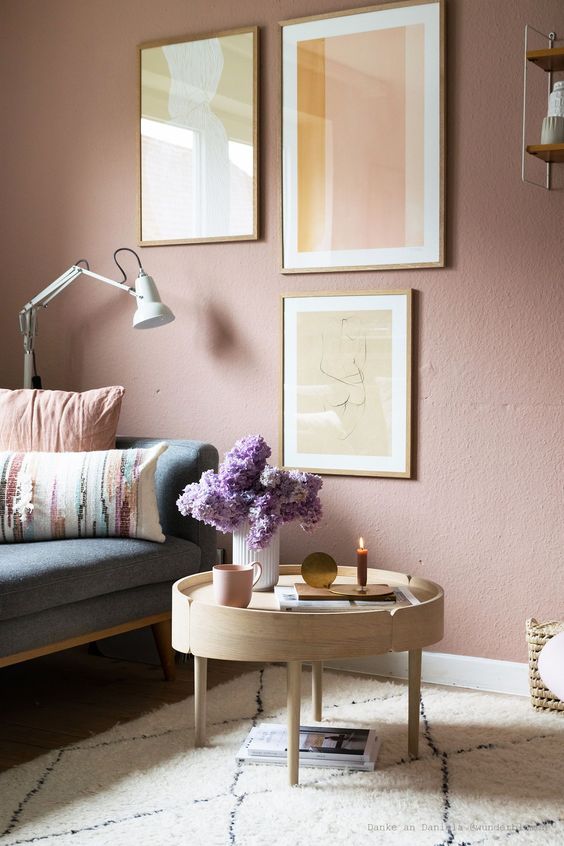 a soothing living room with a mauve accent wall, a neutral and pastel gallery wall and accessories plus a lovely wooden table