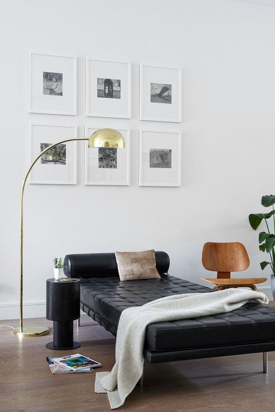 a stylish and polished nook with a grid gallery wall, a black leather daybed, a chair and a side table, a chic floor lamp