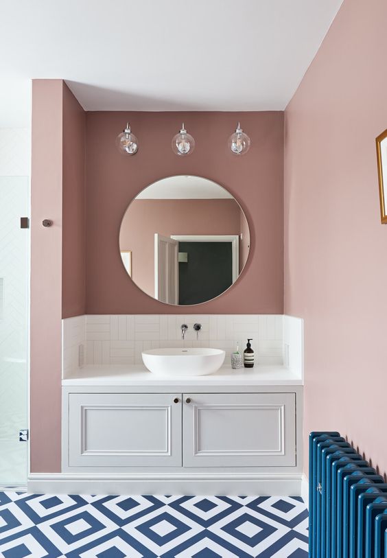 a stylish mauve bathroom with a built in vanity, a round mirror, a blue tiled floor