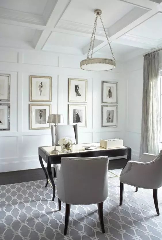 a very elegant and refined neutral home office with paneling and a vintage gallery wlal, a black vintage desk, neutral chairs and a chandelier on chain