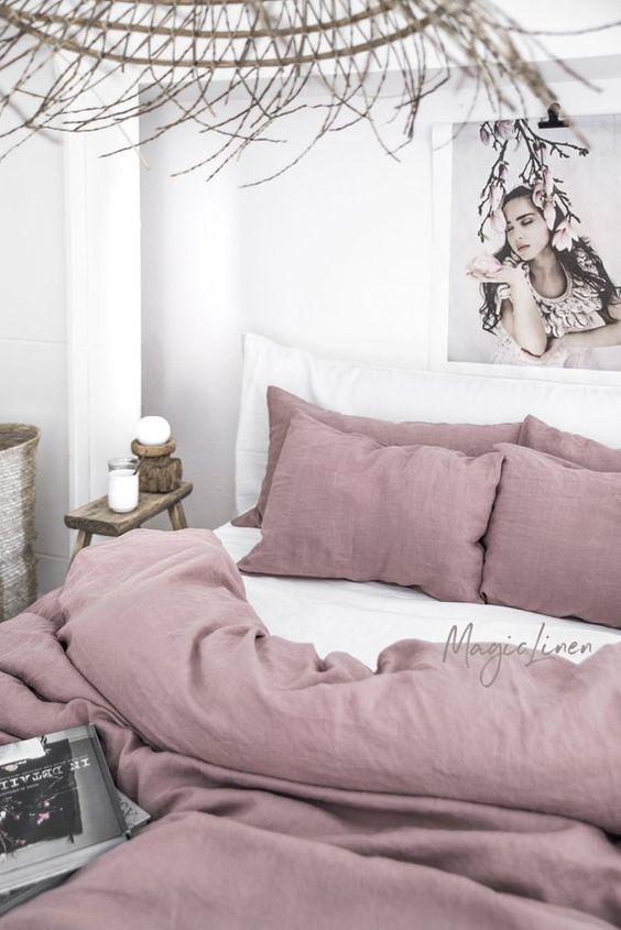 a wabi-sabi neutral bedroom spruced up with white and mauve bedding, a rattan pendant lamp and wooden furniture