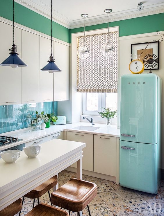 a white L-shaped kitchen with a blue fridge, pendant lamps and patterned tiles on the floor is a pretty and catchy space