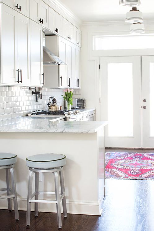 a white farmhouse L-shaped kitchen with white stone countertops and a white subway tile backsplash plus dark handles