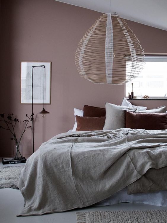 an attic bedroom with a mauve accent wall, green and rust bedding and a stick lamp looks very calming and soothing