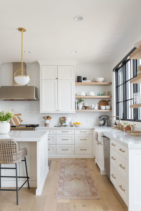 an elegant white L-shaped kitchen with a kitchen island, open shelves, catchy lamps and brass touches