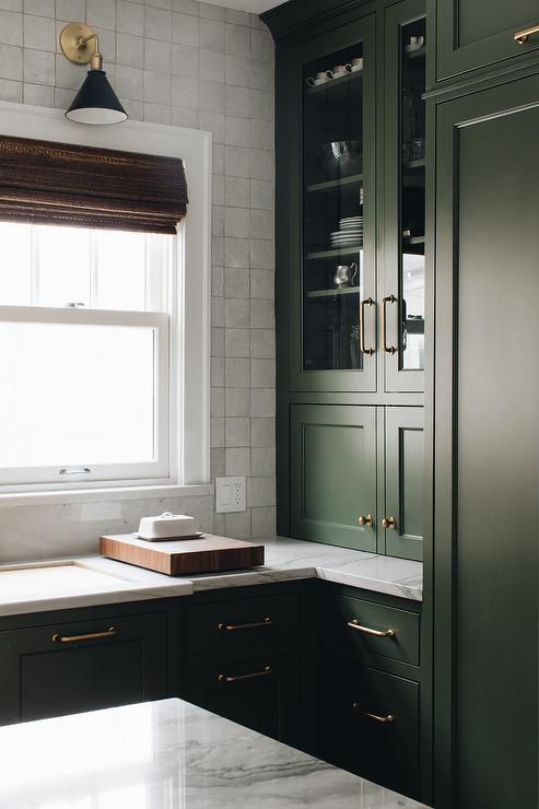 an exquisite dark green kitchen with shaker style cabinets, a white square tile backsplash and white quartz countertops plus a retro lamp