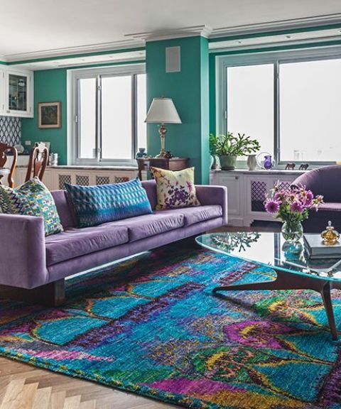 02 a bright living room with green walls, a purple sofa and chairs, a bright rug with purple touches and a glass coffee table