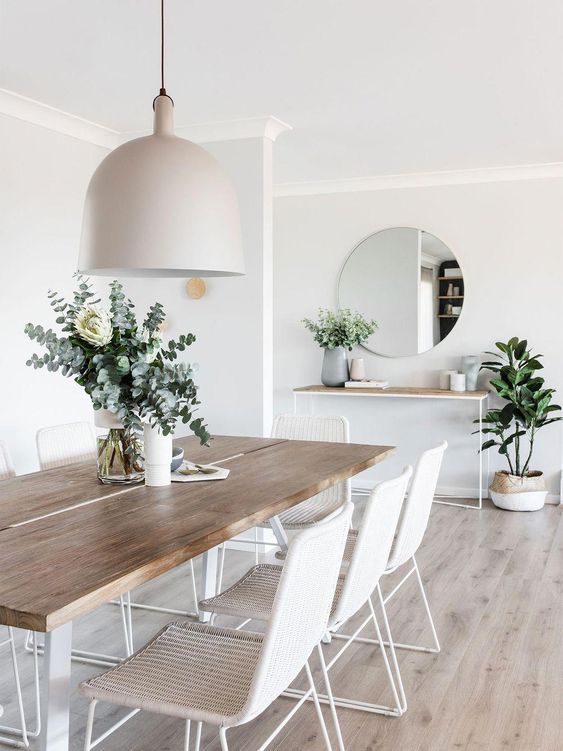 a stylish modern all-neutral dining room with white woven chairs, a sleek table and a console, a pendant lamp and a round mirror
