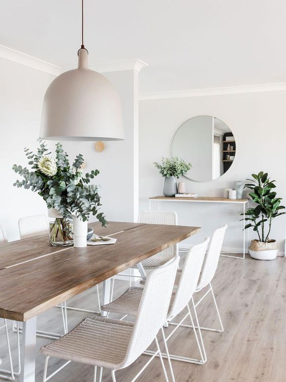 03 a stylish modern all-neutral dining room with white woven chairs, a sleek table and a console, a pendant lamp and a round mirror