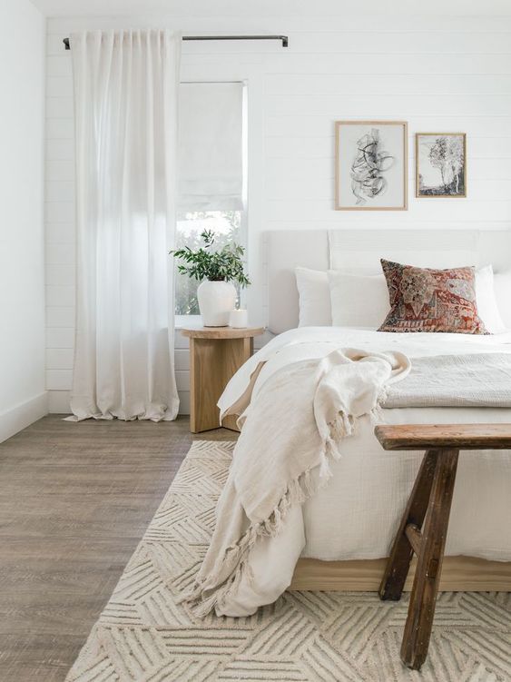 a neutral bedroom with an upholstered bed, a wooden bench and nightstands, neutral textiles and lovely artworks