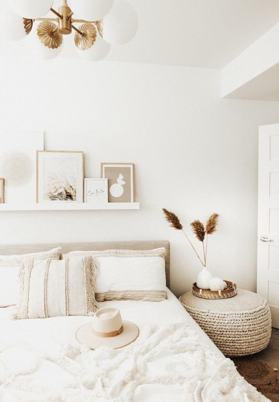 a welcoming and chic neutral boho bedroom with an upholstered bed, a ledge gallery wlal, a woven ottoman and a lovely chandelier