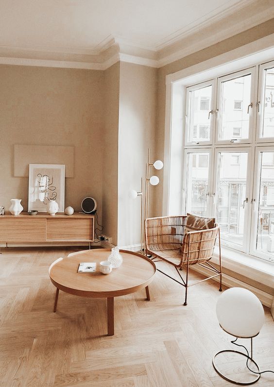 a stylish warm neutral living room with blonde wood and rattan items, with lamps and lots of natural light coming through the window