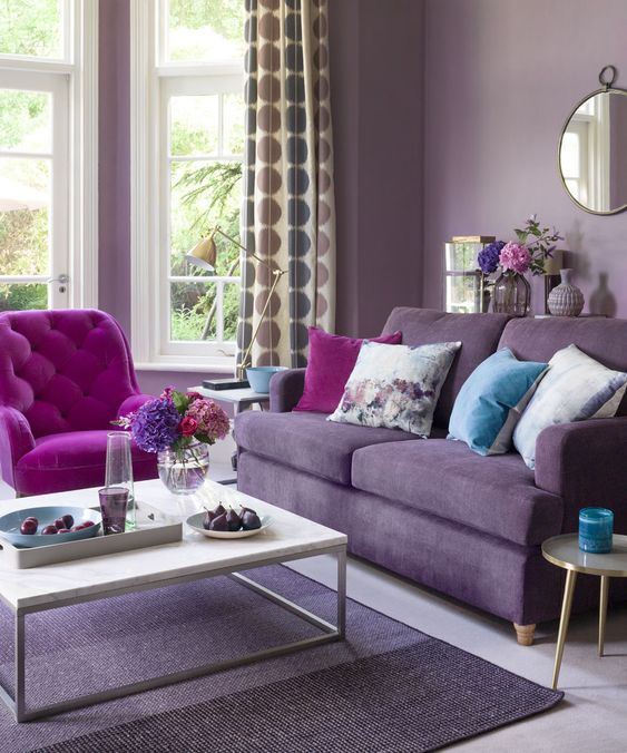 23 a monochromatic living room with lavender walls, a purple sofa, a hot pink chair, floral pillows and printed curtains