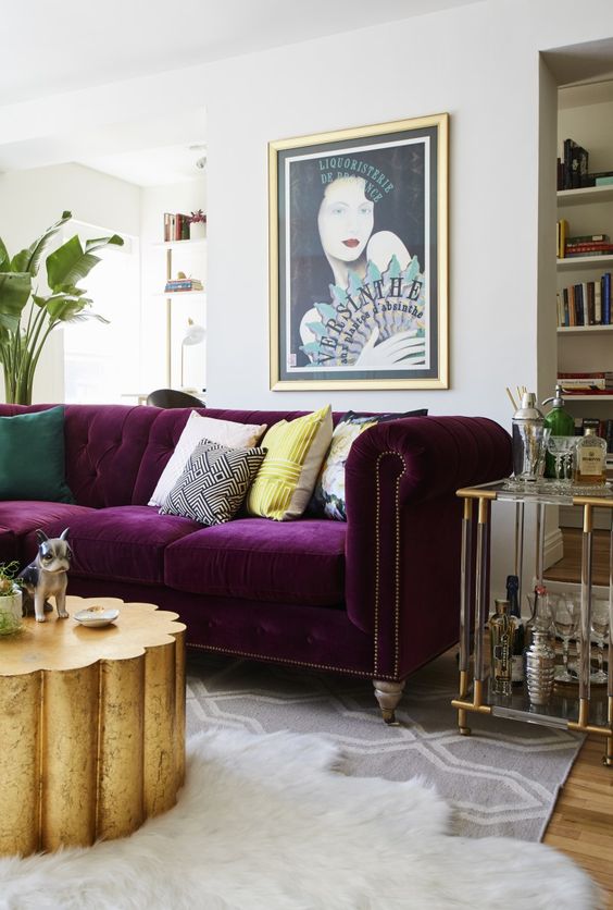 a refined and glam living room in neutrals with a built-in bookcase, a purple sofa, a gold table and an acrylic home bar