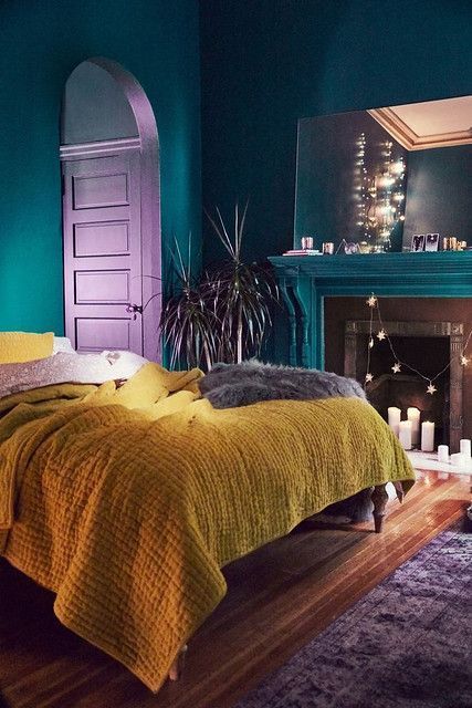 51 a refined bedroom with teal walls, fireplace and a mirror, a bed with mustard bedding and a lilac rug