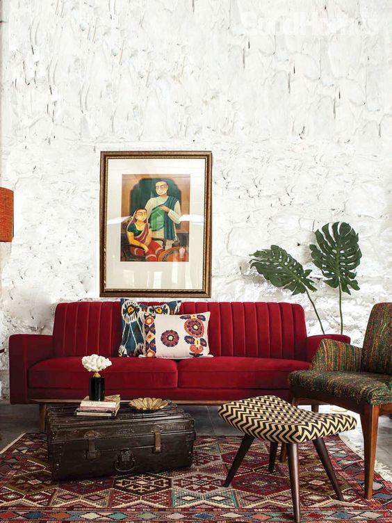 a beautiful living room with catchy walls, a deep red sofa, printed furniture and a rug and a vintage suitcase for storage