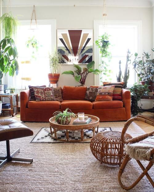 a boho living room with an orange velvet sofa as a centerpiece, potted plants and rattan and leather furniture, boho rugs