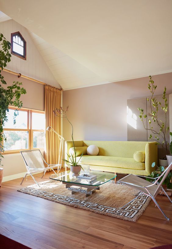 a bold living room with taupe walls, a yellow sofa, modern chairs and a glass table plus potted plants is amazing