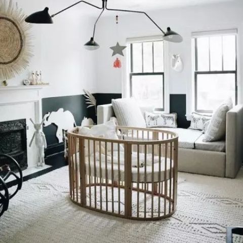 a bold modern nursery with black and white walls, a grey couch and a light stained crib, a faux fireplace, a black chandelier and cool decor