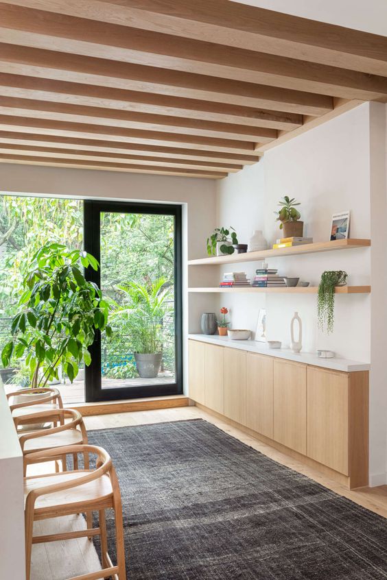 a chic mid-century modern space with a blonde wood credenza, chairs, shelves and wooden beams on the ceiling