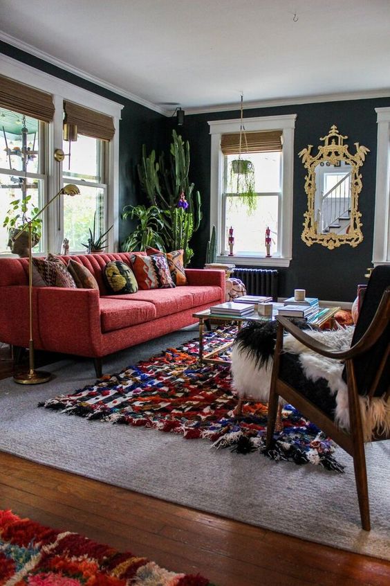 a chic modern living room with graphite grey walls, a red sofa, a colorful rug, a black chair and potted cacti is wow