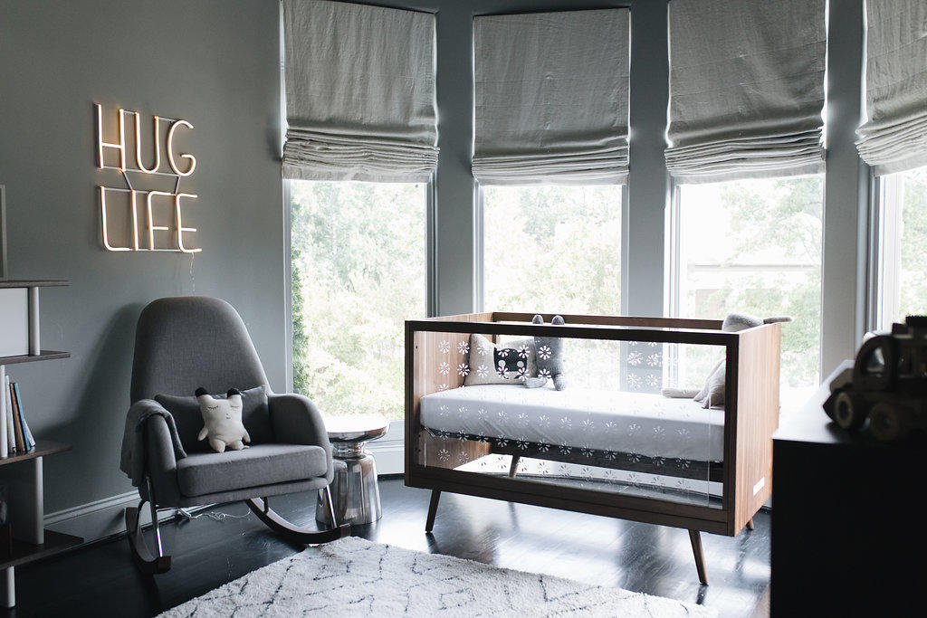 a chic modern nursery in greys with grey walls and curtains, a grey rocker, a wood and acryl crib and some cool storage units