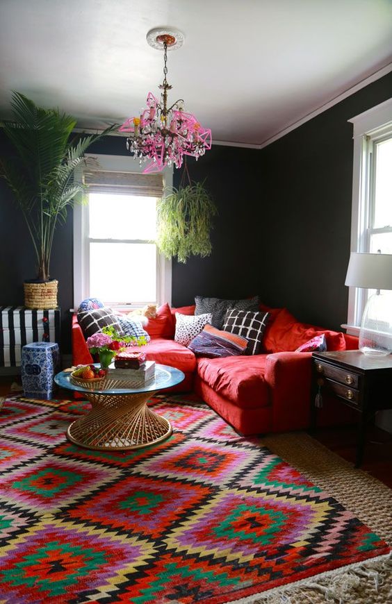 a colorful living room with black walls, a red sofa, a bold rug, a pink chandelier and some potted plants is amazing