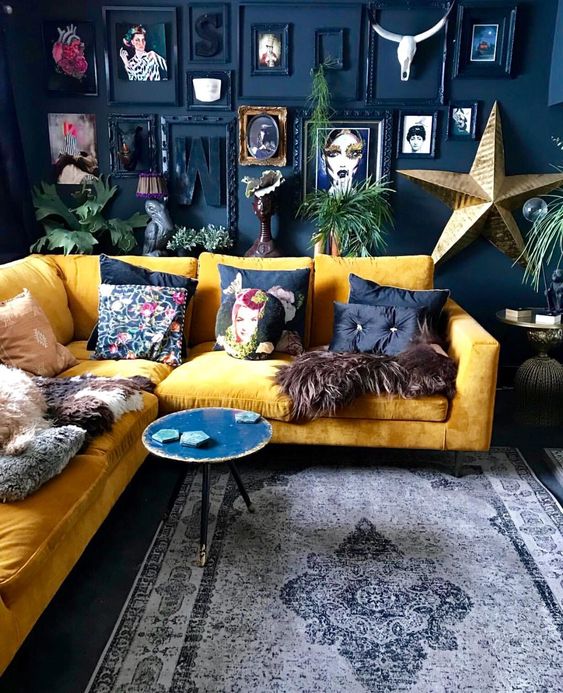 a dramatic living room with a navy accent wall, a bold gallery wall, a yellow sectional and bright pillows plus a round table