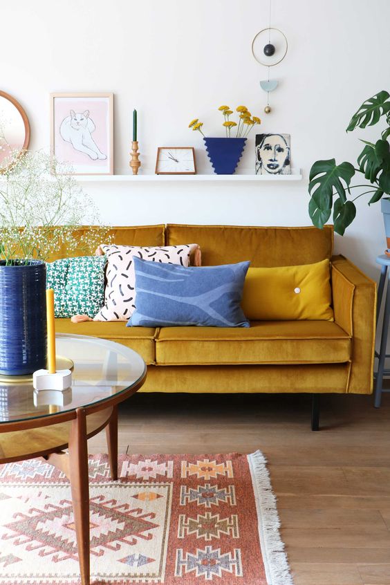 a lively living room with a mustard sofa, a round table, a ledge gallery wall and touches of blue for a contrast