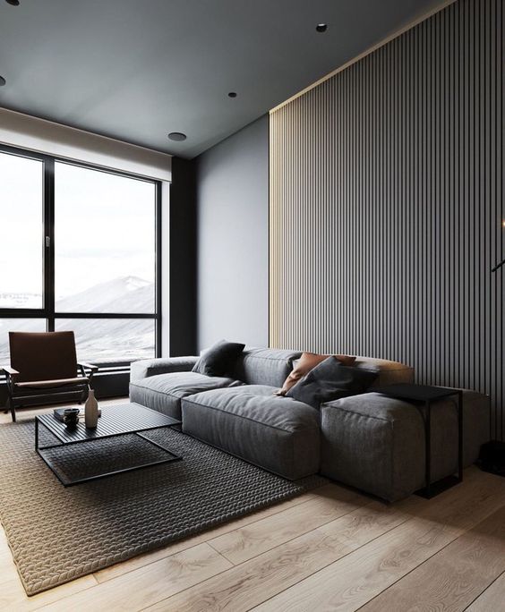 a minimalist living room with a slab wall, a grey low sofa, a leather chair and a low metal coffee table