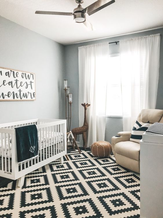 a modern black and white nursery with neutral furniture, grey walls, printed textiles and a graphic artwork plus a leather pouf