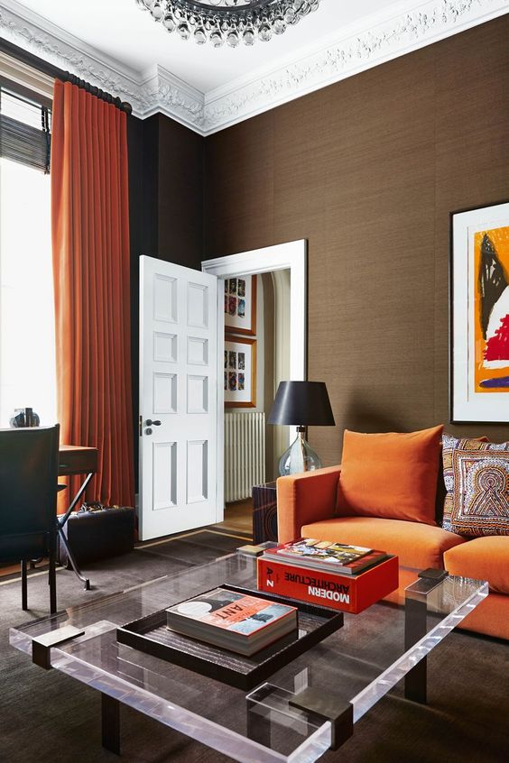 a modern living room with an orange sofa, a low acrylic table, a desk and a leather chair plus a crystal chandelier