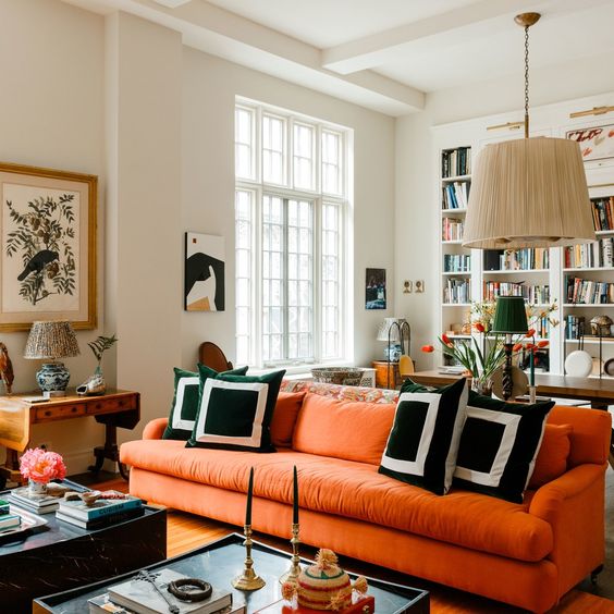 a modern living room with an orange sofa, a pendant lamp, graphic pillows, some coffee tables and lovely artworks