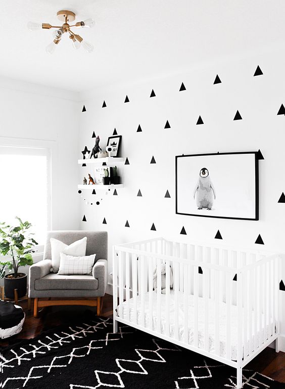 a modern monochromatic nursery with a geo printed wall, a printed rug, a white crib, a grey chair and a potted plant