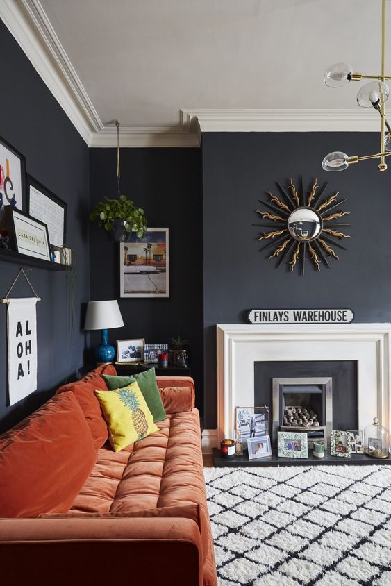 a moody living room with a faux fireplace, artworks, prints and candles, a rust-colored sofa and a pretty gallery wall