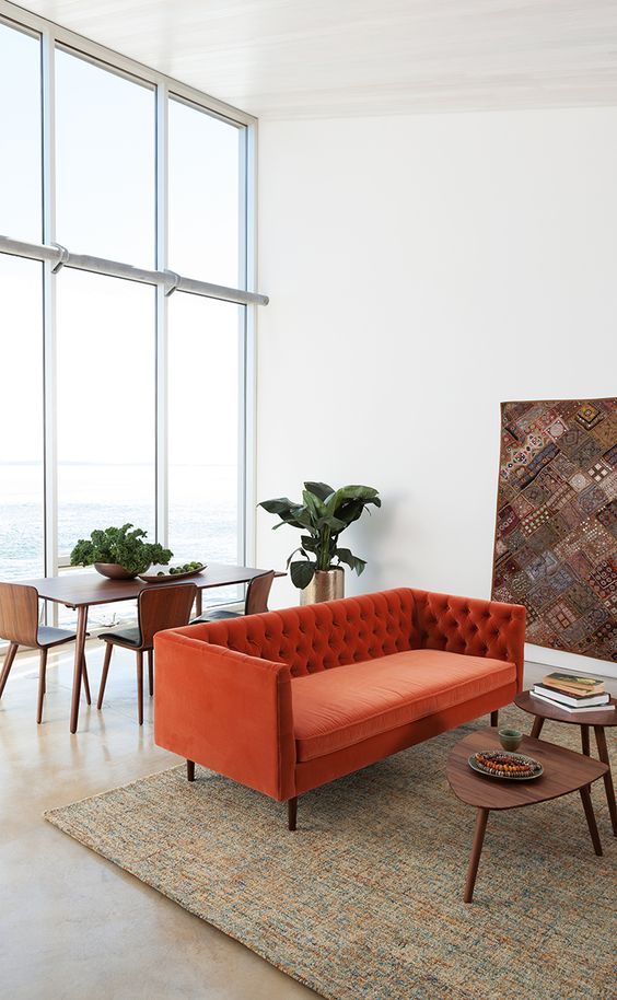 a neutral double height ceiling space, with an orange sofa, a duo of tables and a dining zone by the window