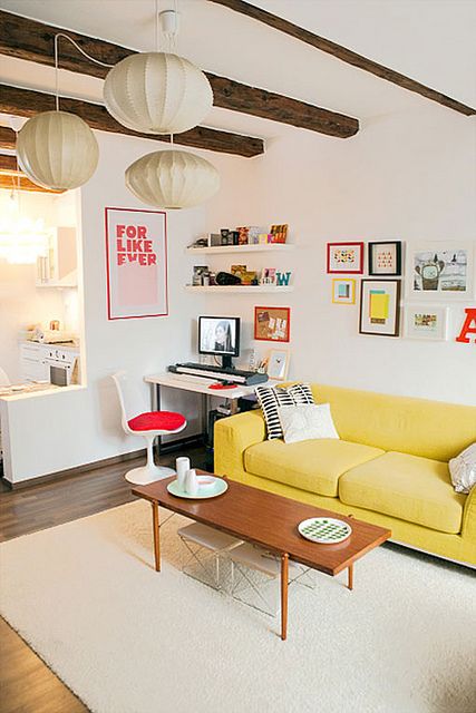 a pretty white living room with wooden beams, a bright gallery wall, a working space and a yellow sofa lit up by paper lamps