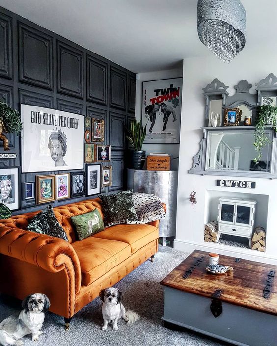 a quirky living room with a black paneled wall, an orange sofa, a mini hearth and a mirror, a whimsy gallery wall and a low table