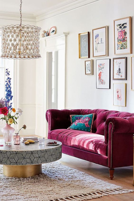 a refined living room with a pink tufted sofa, a gallery wall, a geometric and gold table, a floral chandelier is wow